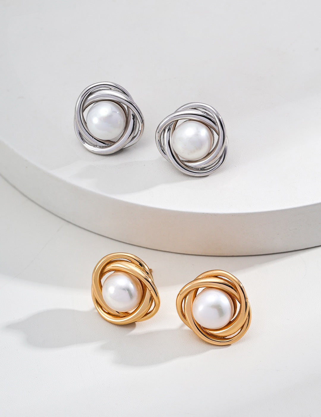 A close-up image of two pairs of pearl stud earrings displayed on the white stage.