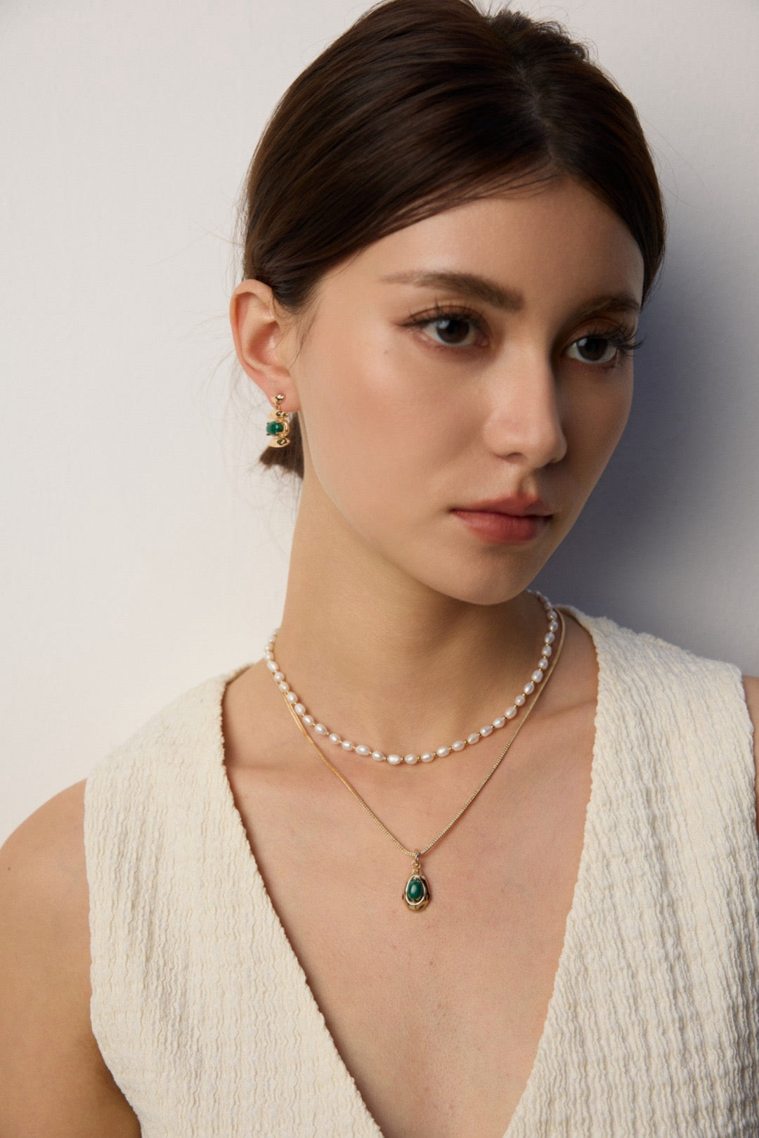 Woman wearing a pearl necklace with a pendant against a neutral background