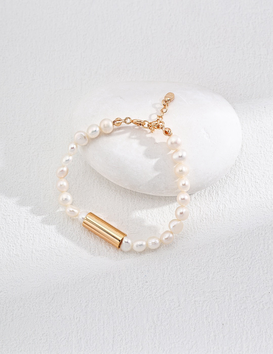 A bracelet with pearl beads and an 18k gold vermeil chain placed on a white rock, with a white background.