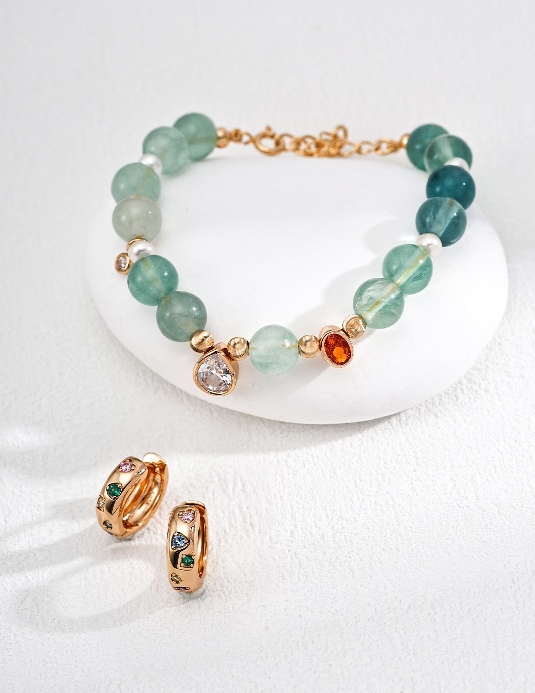 Bracelet with green aquamarines, zircon charm and gold accents on a white surface