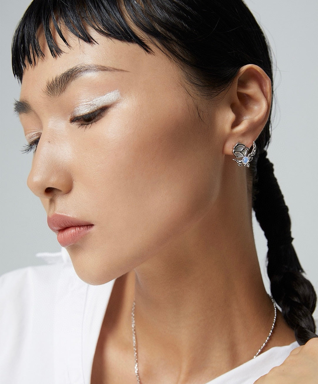 Close-up of a woman wearing asymmetrical butterfly earrings with a neutral background