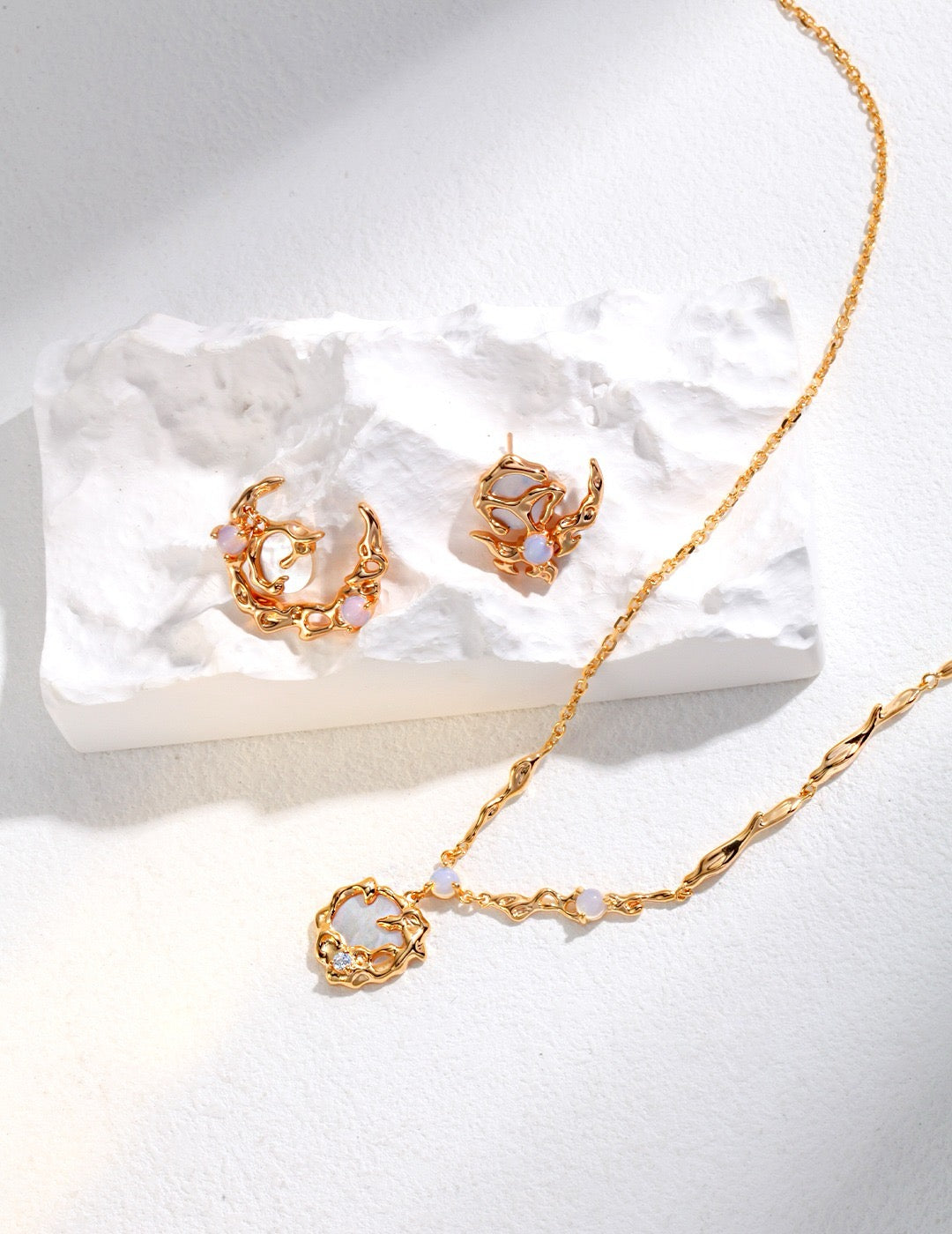 Gold necklace and earrings on a white stone surface