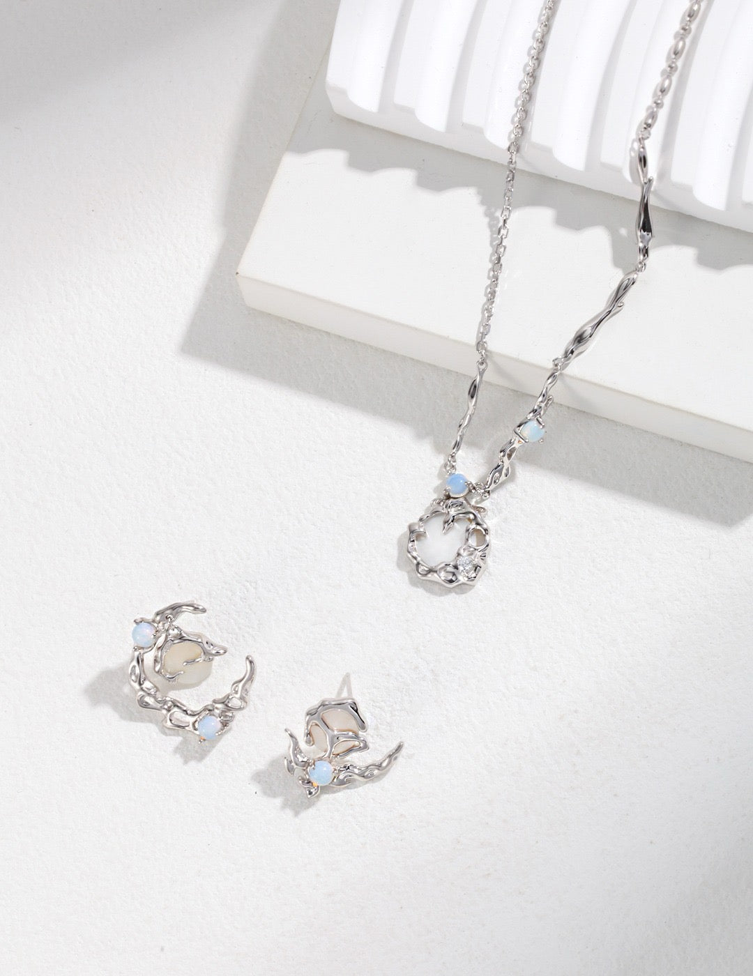 Silver jewelry set with necklace and asymmetrical earrings on a white surface