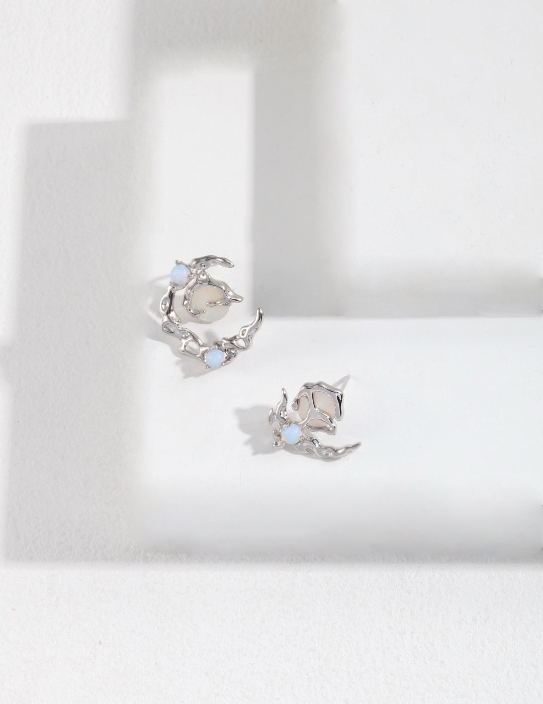 Pair of asymmetrical silver earrings with gemstones on a white background