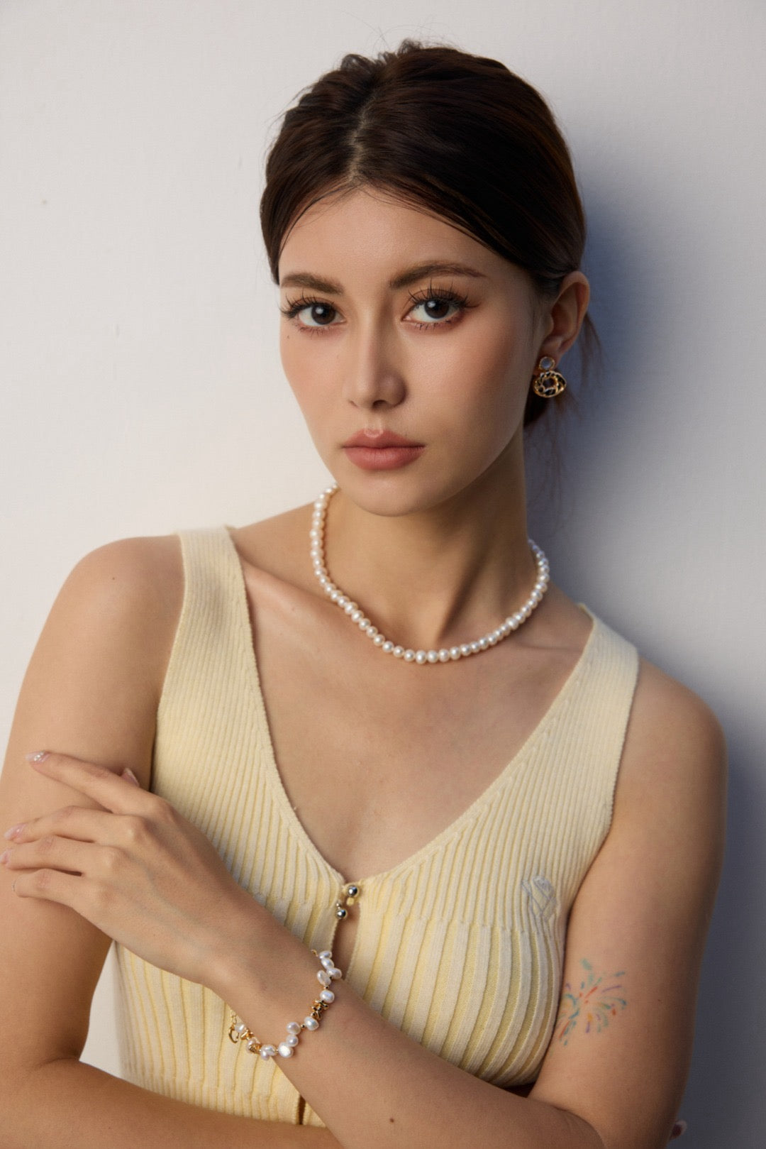 Woman wearing a yellow dress with a pearl strand necklace and bracelet against a plain background