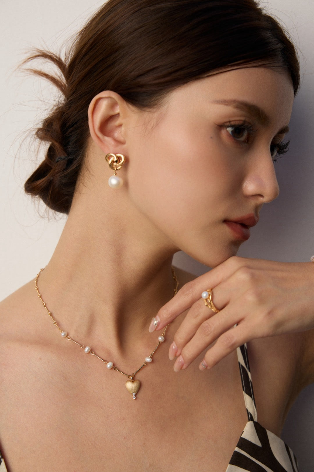 Woman wearing gold pearl jewelry, including earrings, necklace, and ring, on a neutral background