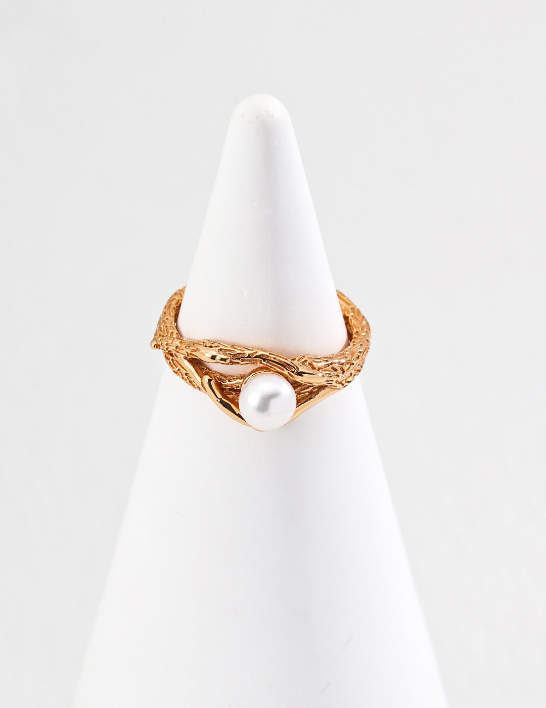 Gold pearl ring with a pearl on a white stand against a light gray background