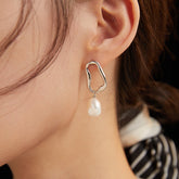 A close-up image of a person wearing a silver hoop earring with a baroque pearl drop design.