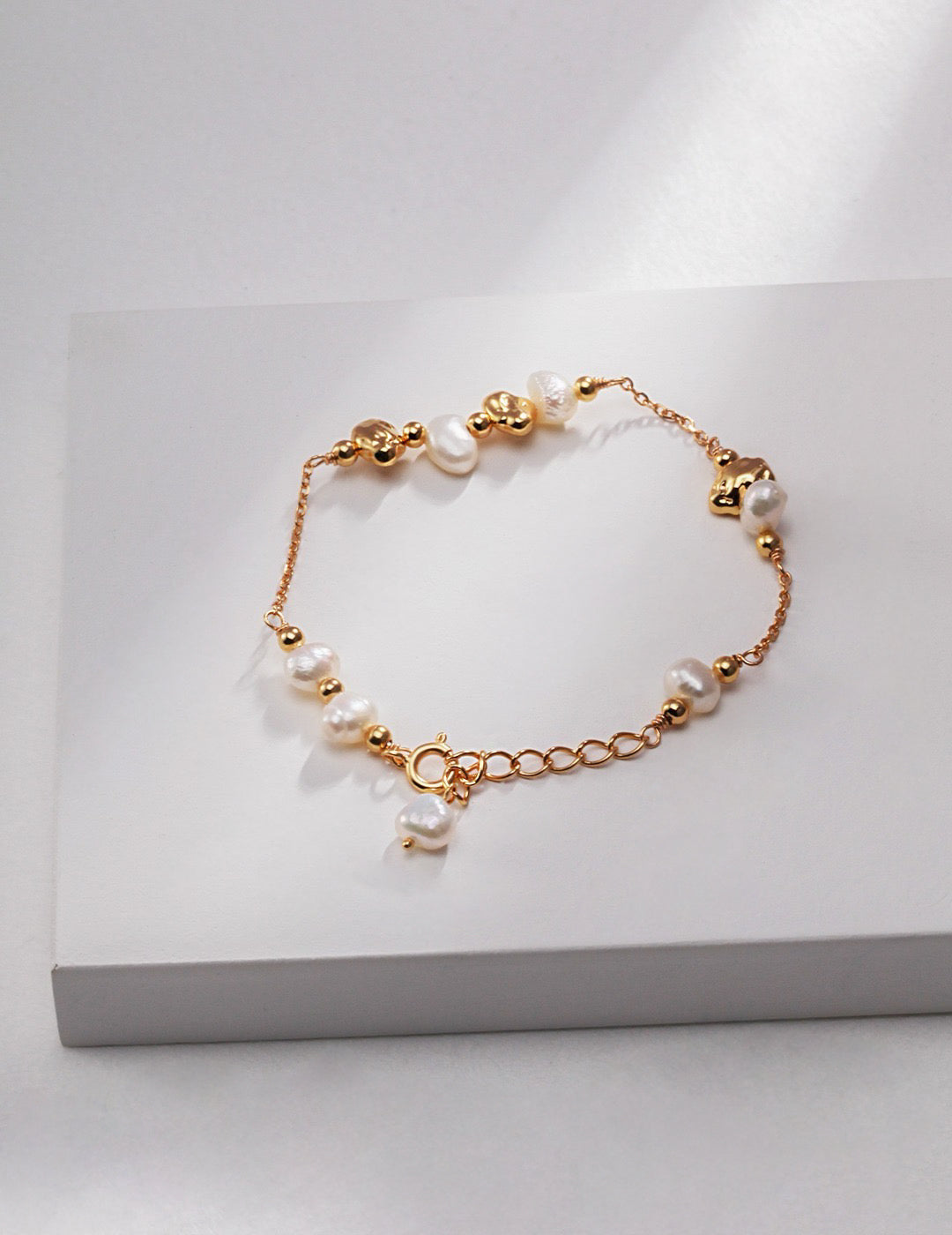 Minimalist gold bracelet with pearls on a white surface