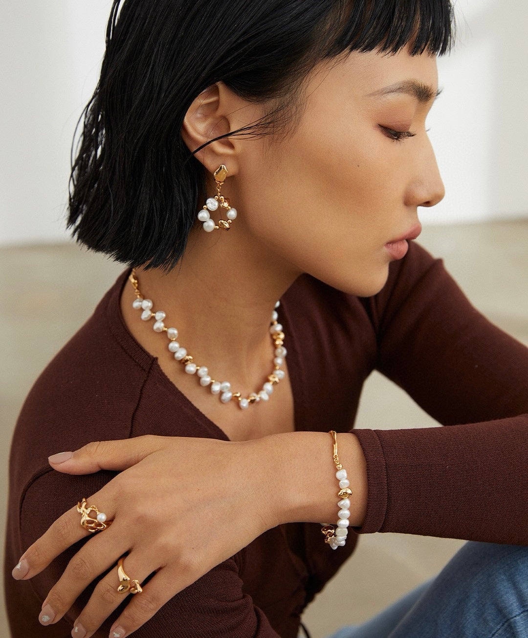Woman wearing pearl jewelry including earrings, necklace, and bracelet with a neutral background