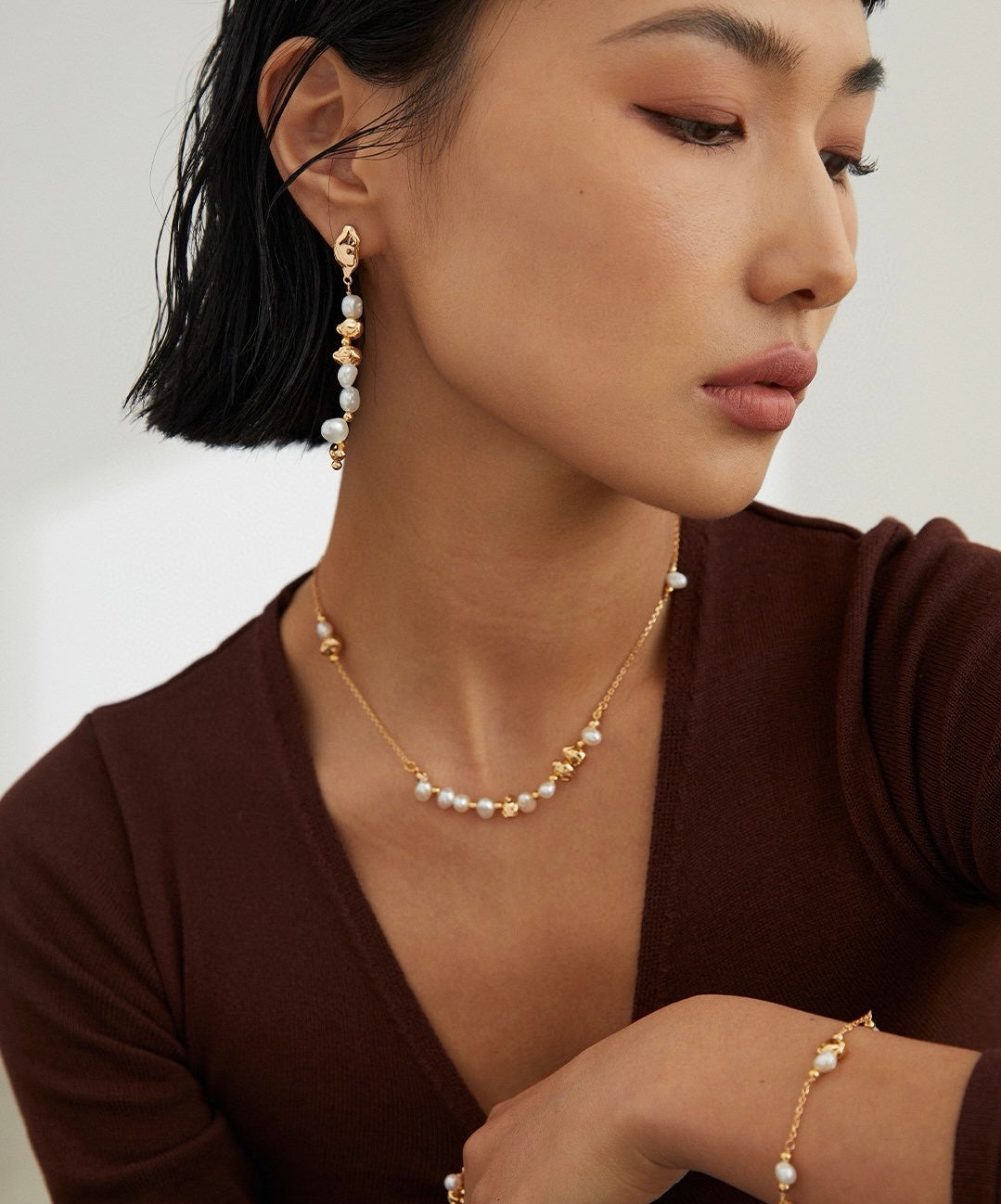 Woman wearing a minimalist pearl necklace and earrings with a neutral background