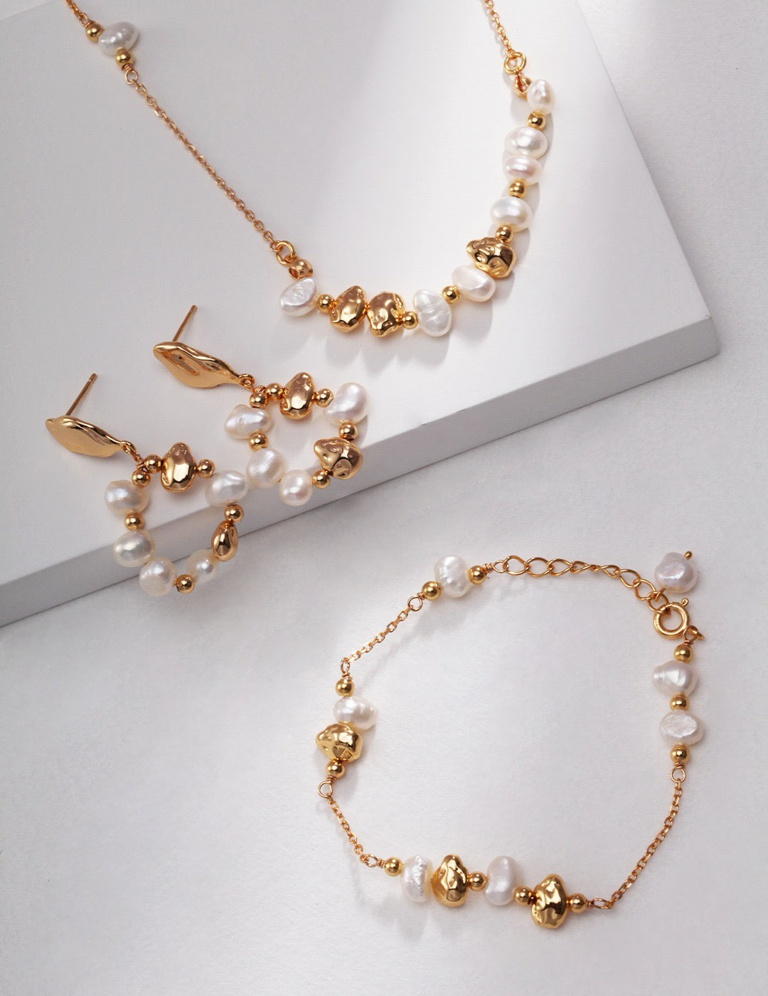 Gold and pearl jewelry set, including necklace, earrings, and bracelet on a light gray background
