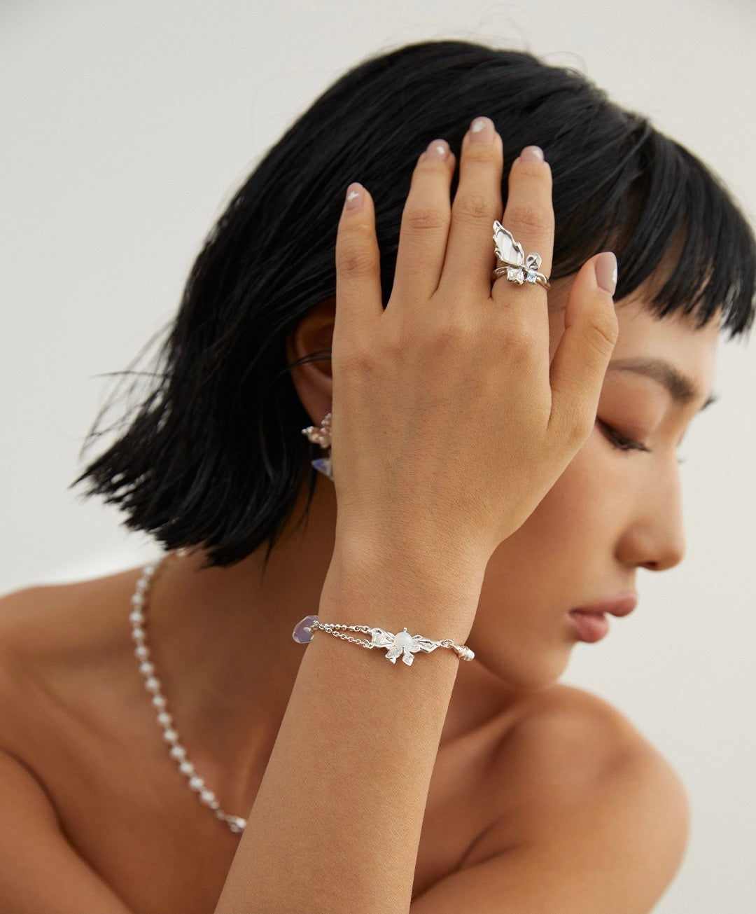 Woman wearing a silver bracelet and ring on a plain background