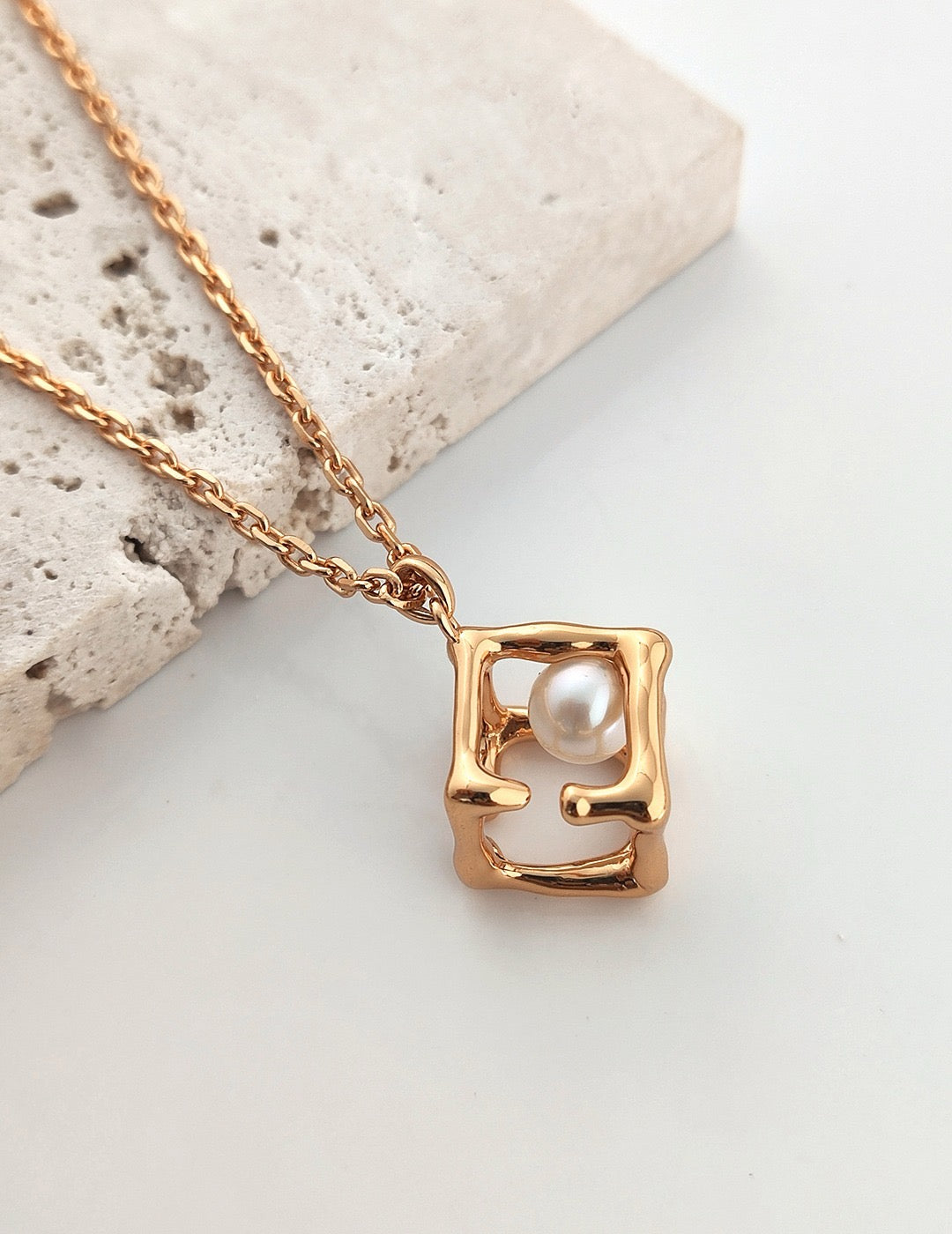 Aurora Cage Pearl Necklace in 18K Gold Vermeil, featuring a freshwater pearl inside an abstract gold vermeil displayed on the rock