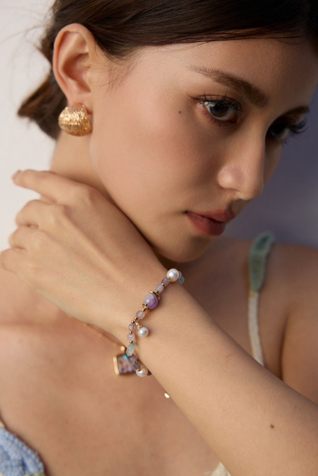 Woman wearing gold earrings and a colorful bracelet on a plain background