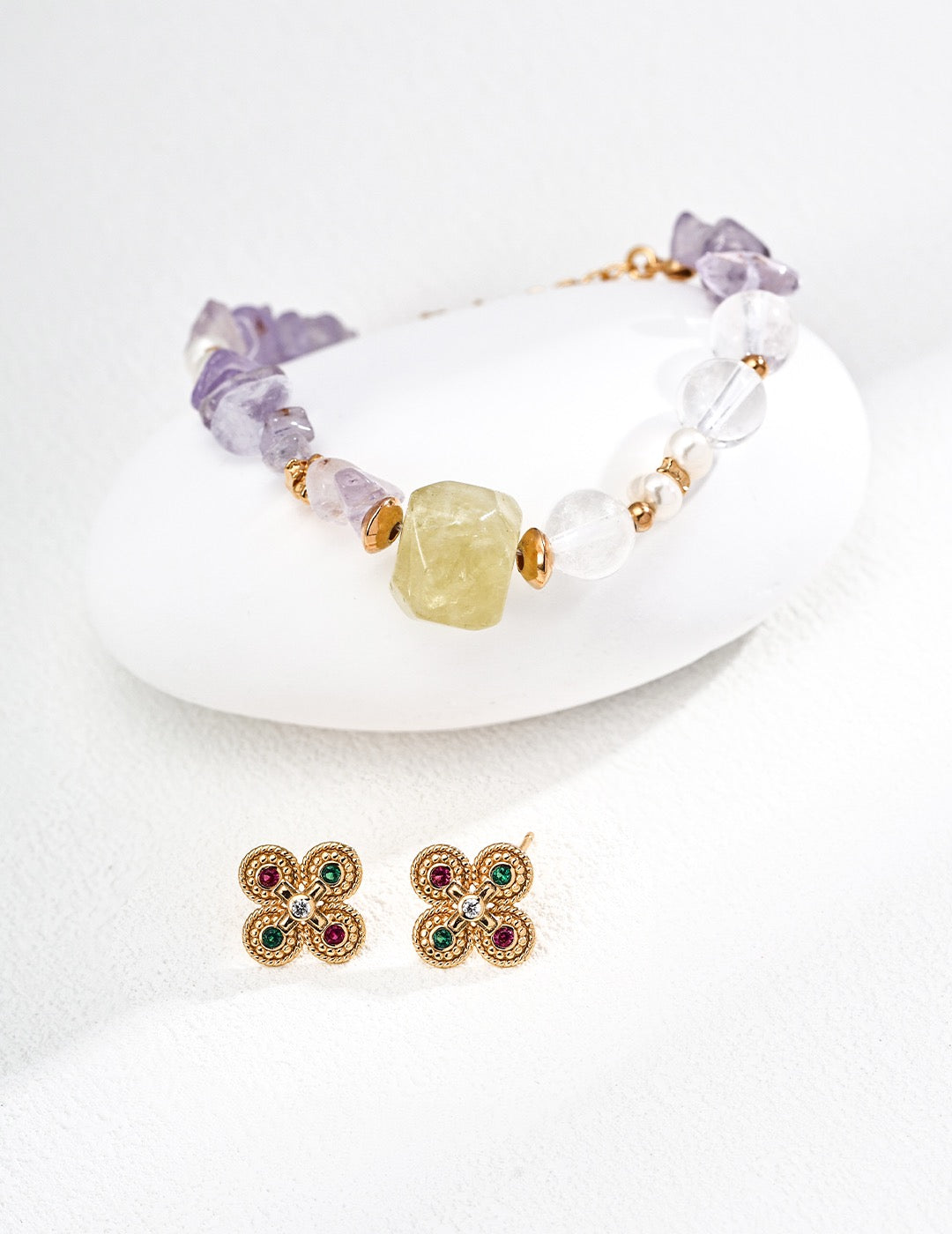 Gemstone Bracelet with Natural Amethyst, Citrine, Rose Quartz & Pearl display on a white rock, accompanied by green and red gemstone earrings.