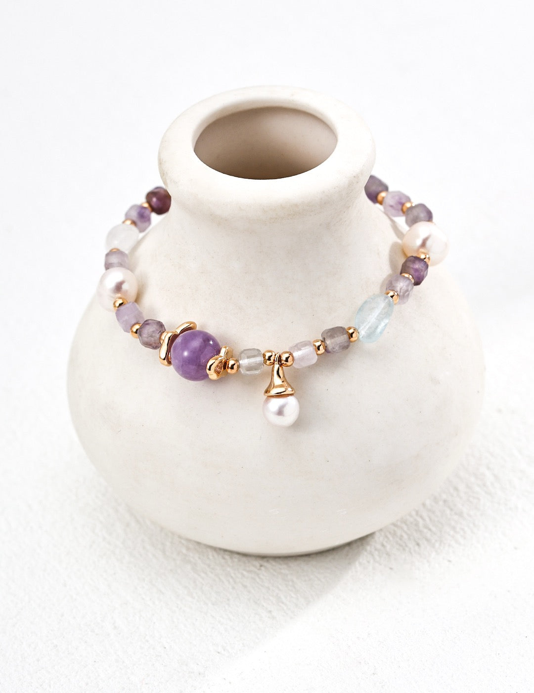 Elegant Aurora gemstone bracelet with amethyst, aquamarine, freshwater pearls, and gold vermeil accents, draped over a white ceramic vase for a minimal aesthetic.
