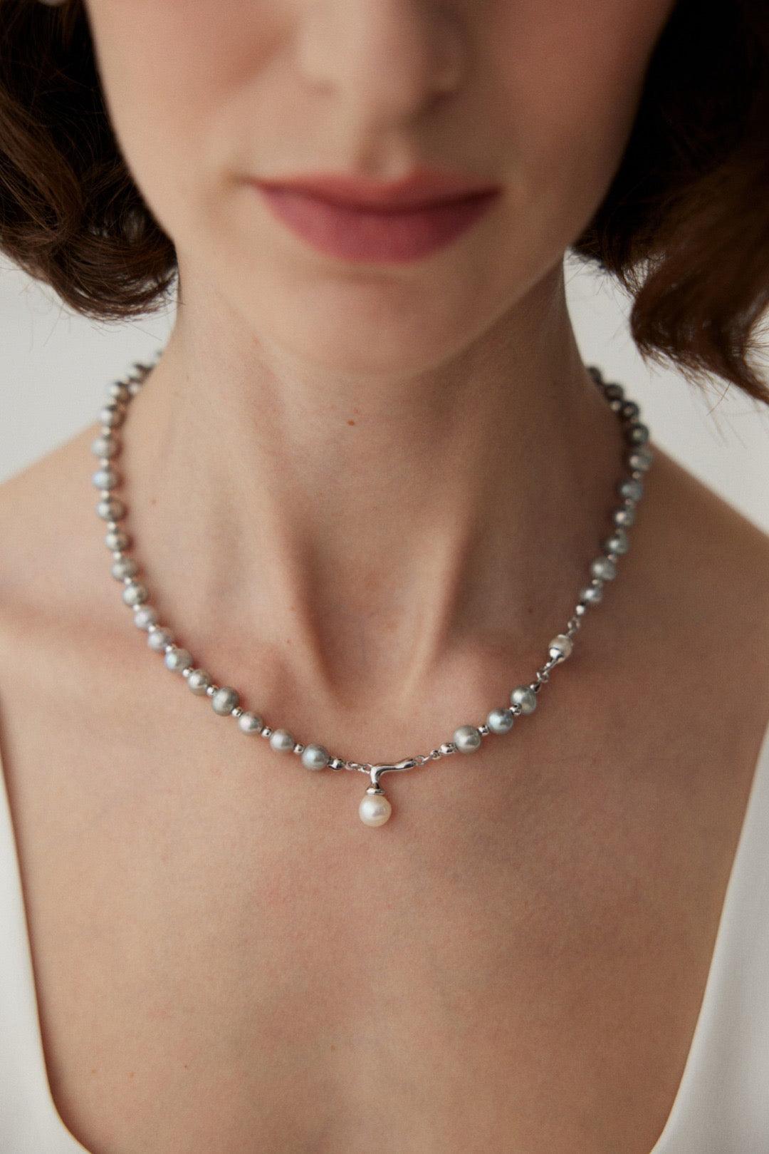 A woman wearing an Ava Pearl Pendant Necklace with a silver chain and a pearl pendant.