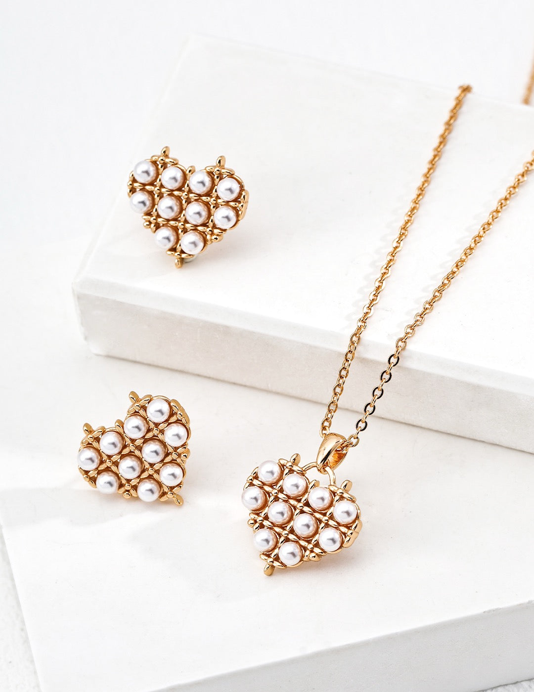 Gold heart-shaped jewelry set with pearls on a white surface