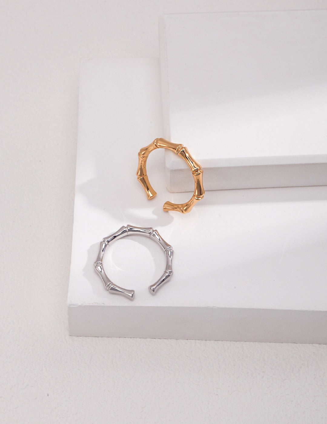 Two rings with a bamboo design, one in gold and the other in silver, are displayed on a white surface.