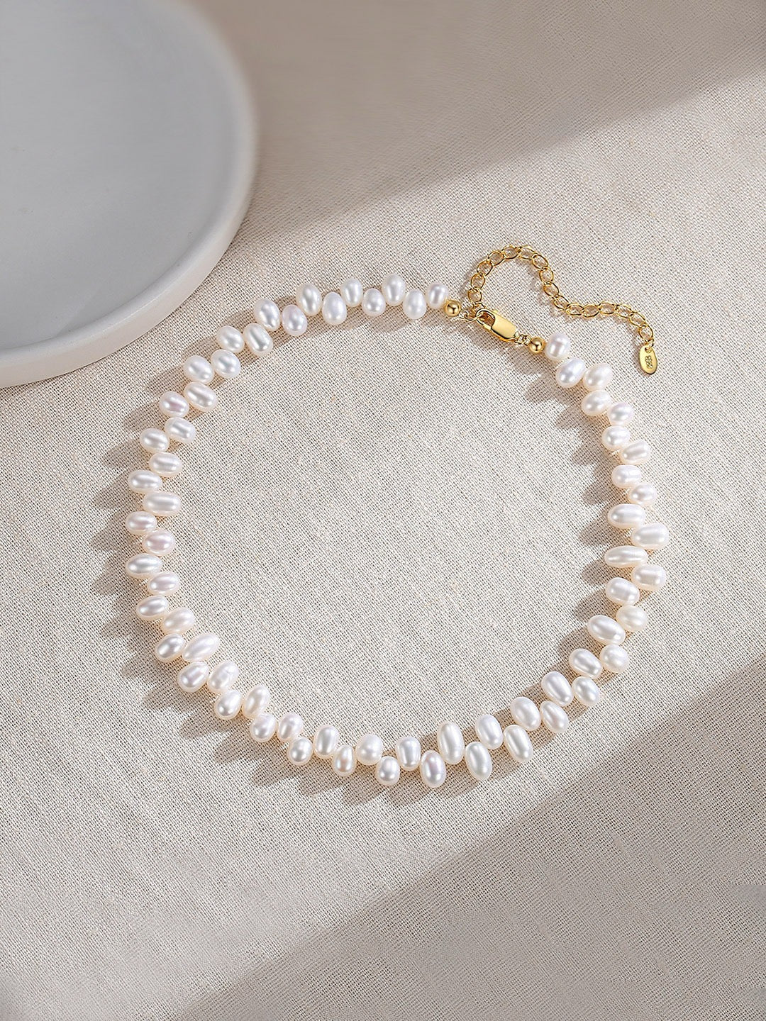 Pearl necklace in gold clasp on a light fabric surface with a neutral background