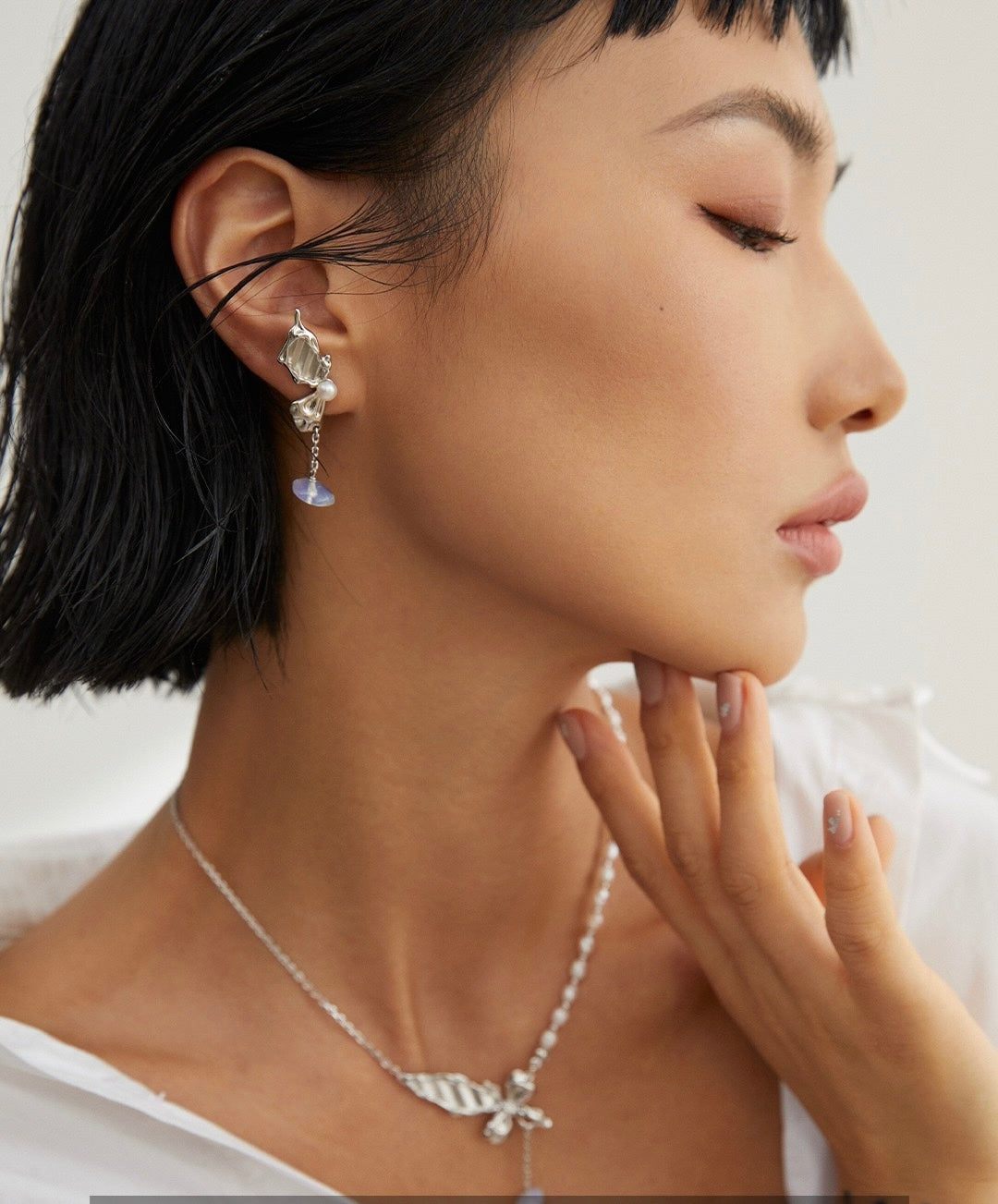Close-up of a woman wearing silver butterfly earrings and a necklace against a neutral background