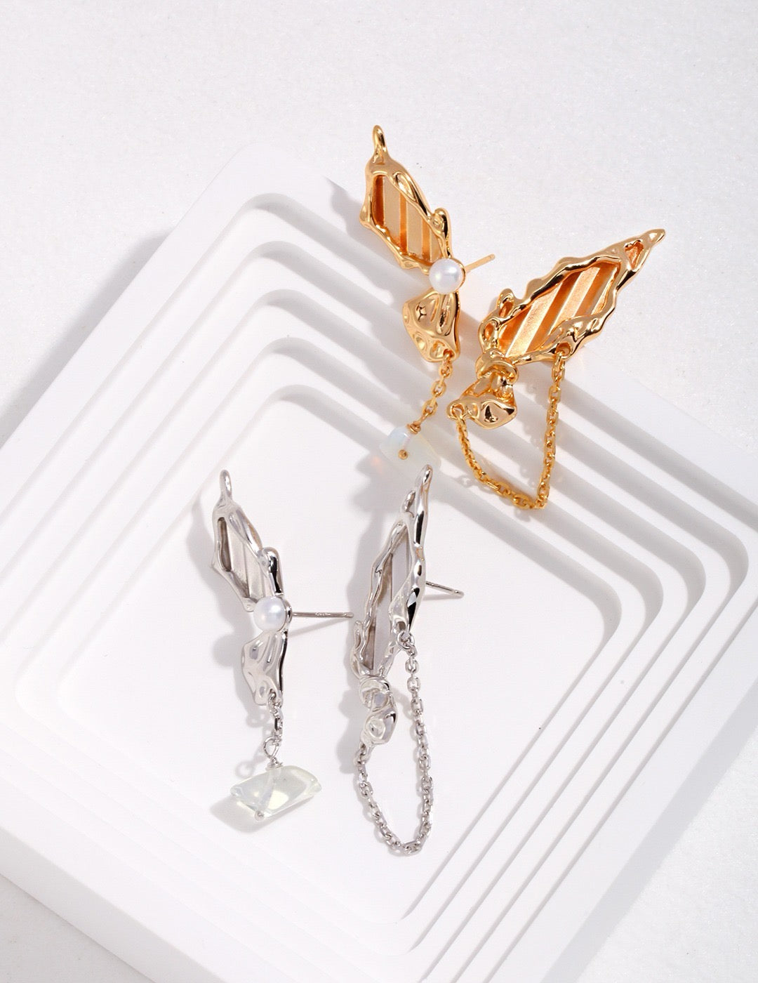 Gold and silver butterfly asymmetrical earrings on a white background