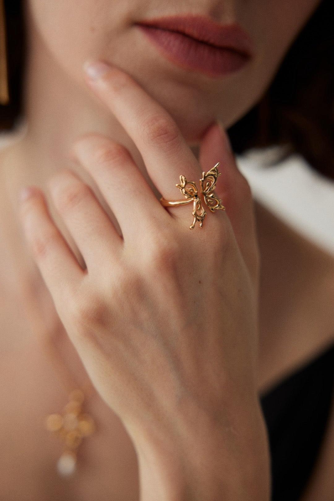 A close-up image of a person wearing an 18k gold vermeil open ring with a butterfly motif on their finger.