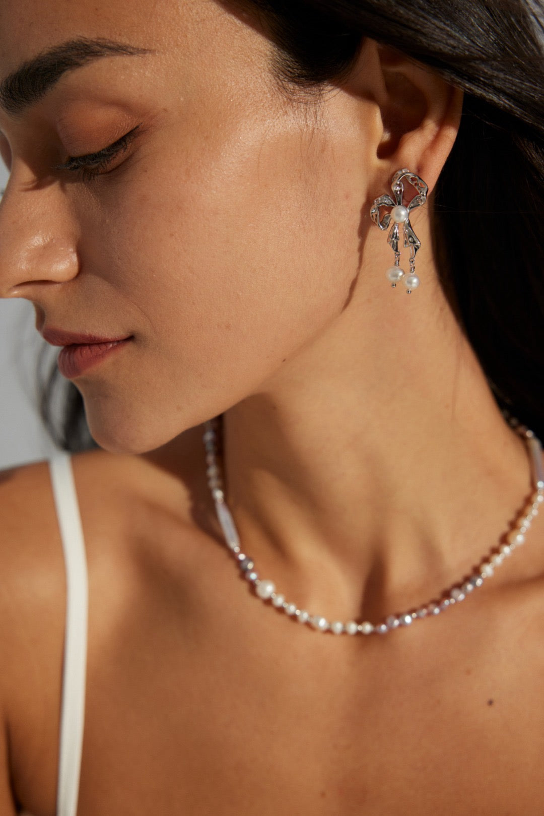 A woman wearing a pair of butterfly-shaped pearl earrings attached to a post, crafted in 18K gold vermeil and sterling silver.