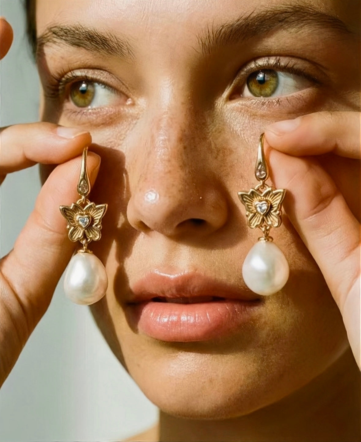 Model holding a pair of butterfly pearl drop earrings in 18k gold