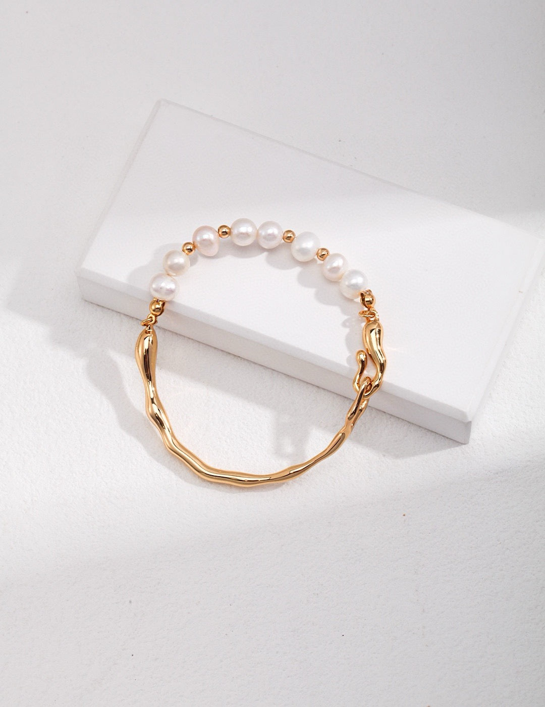 Front view of the Caitlin Minimalist Pearl Asymmetrical Bracelet In 18K Gold, displayed on the white block, showcasing the lustrous pearl.
