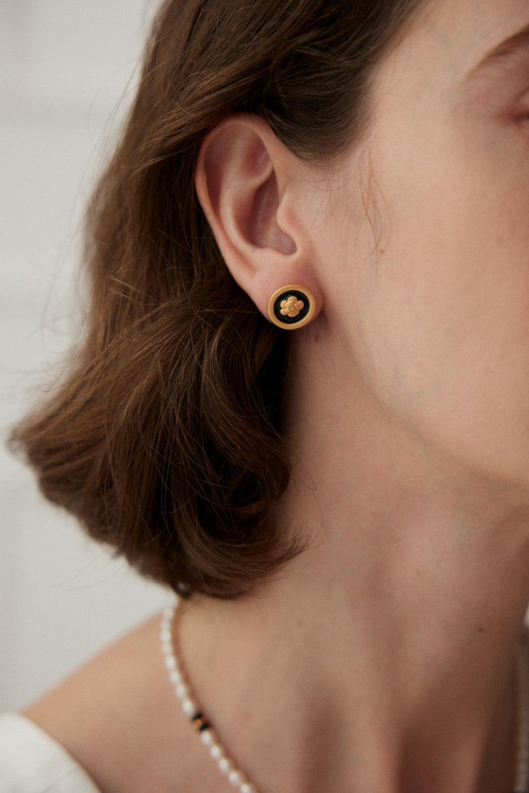A person wearing a pair of gold vermeil camellia stud earrings on their ears.