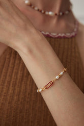A person wearing the Cecily Bracelet, which features white Freshwater pearls and red enamel link accents on a gold vermeil band.