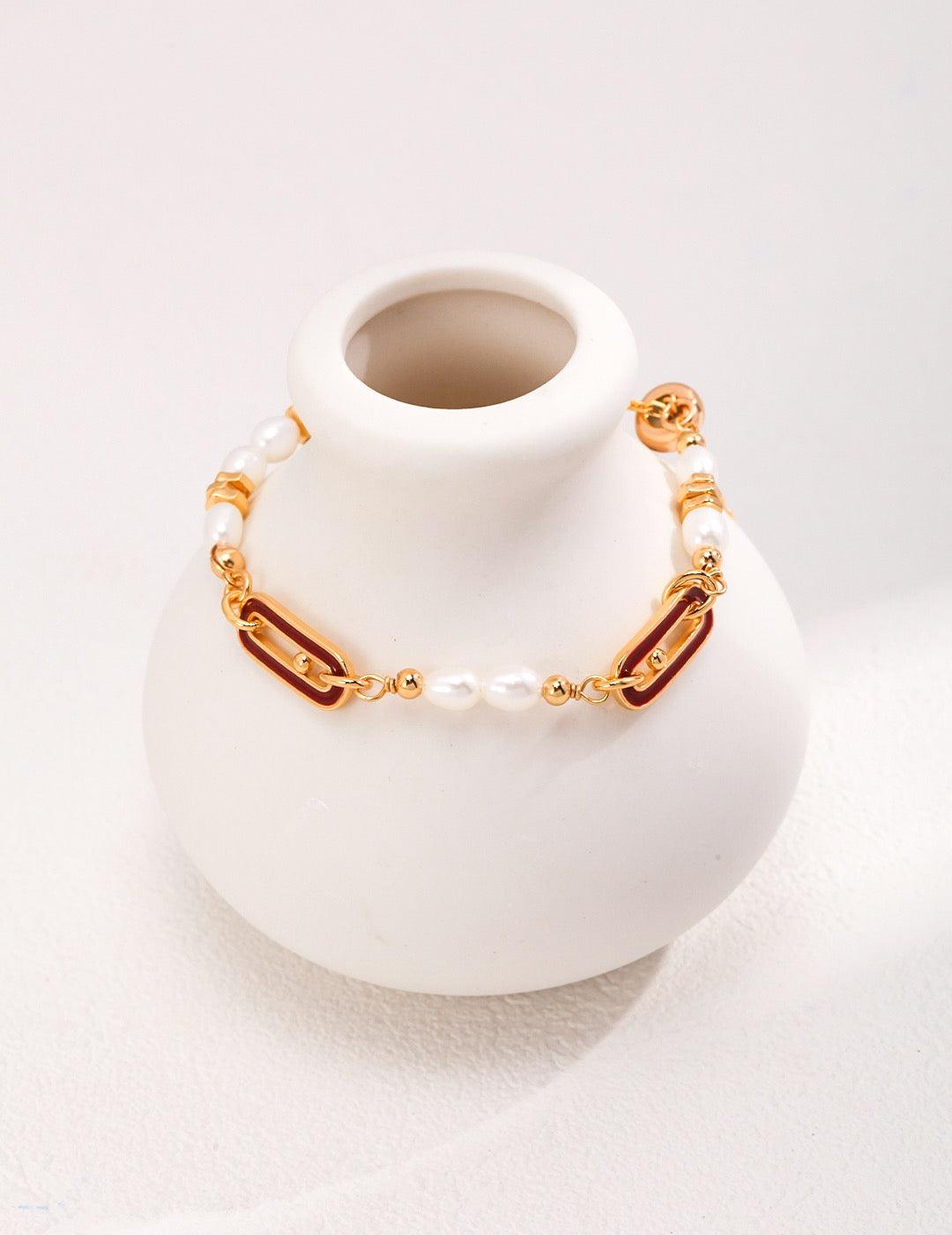 The Cecily Bracelet showcases lustrous 4.5-5mm freshwater pearls elegantly interspersed with distinctive red enamel link accents and gleaming 18K gold vermeil beads displayed on the white vase.