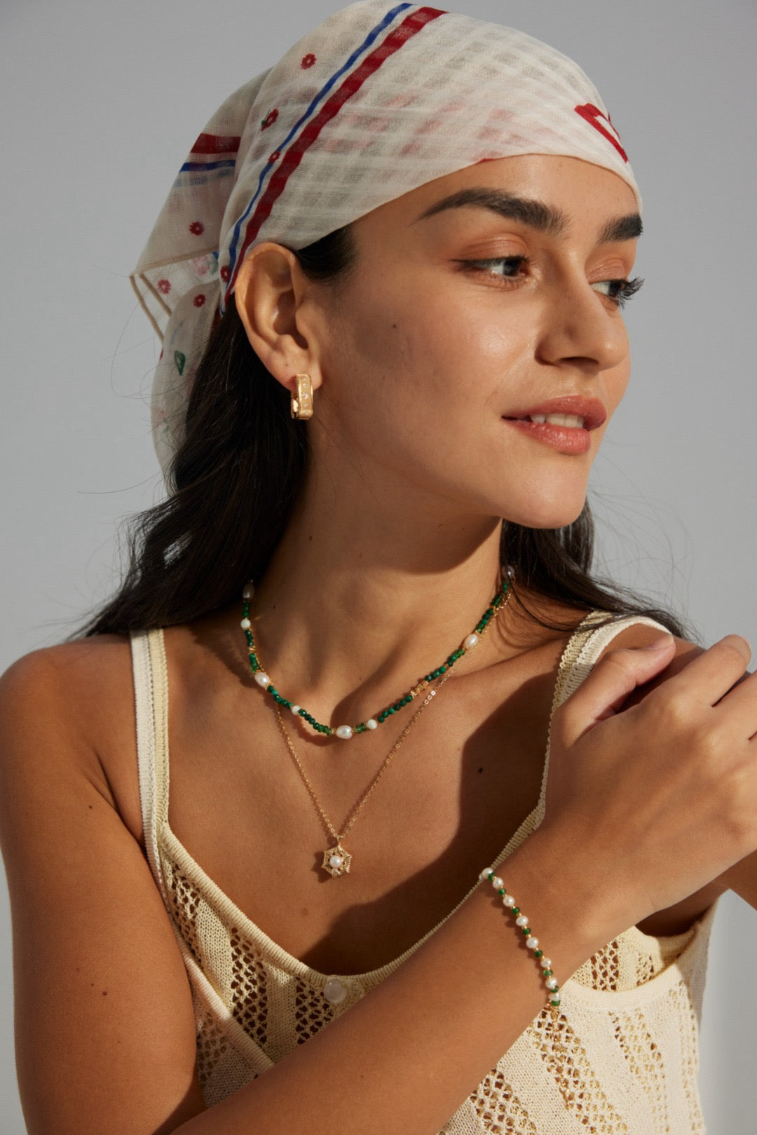 Woman wearing a headscarf and jewelry against a plain background