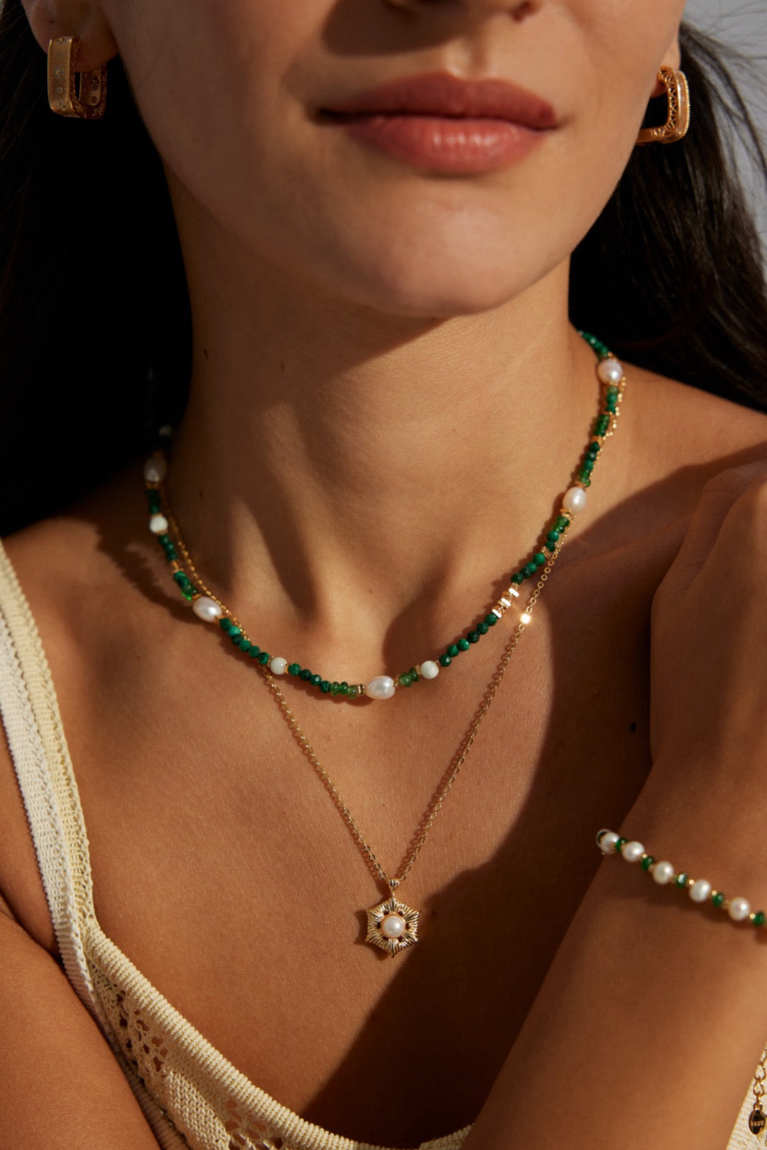 Close-up of a person wearing gold necklaces with green and white beads.