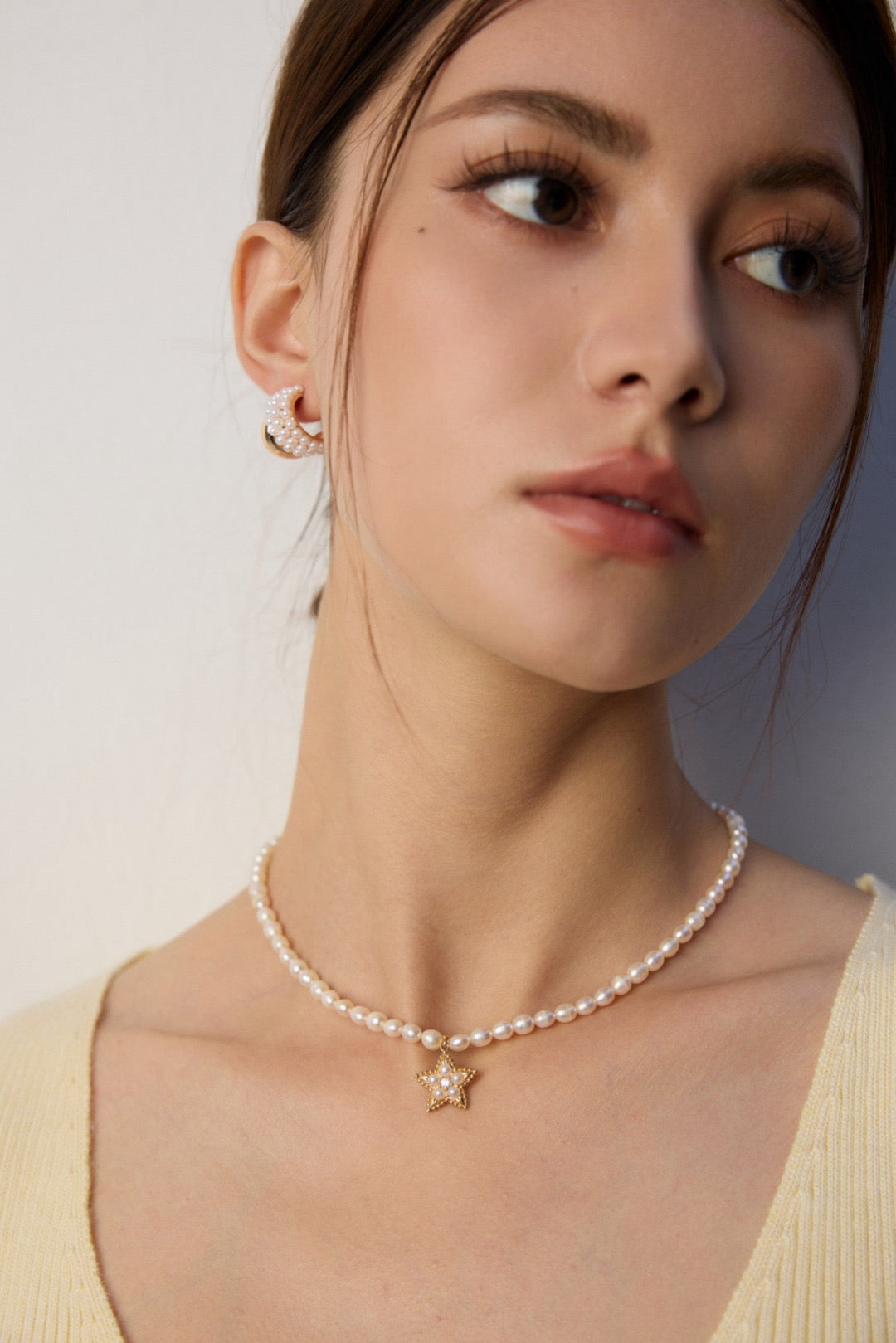 Woman wearing a pearl necklace with a star pendant against a neutral background