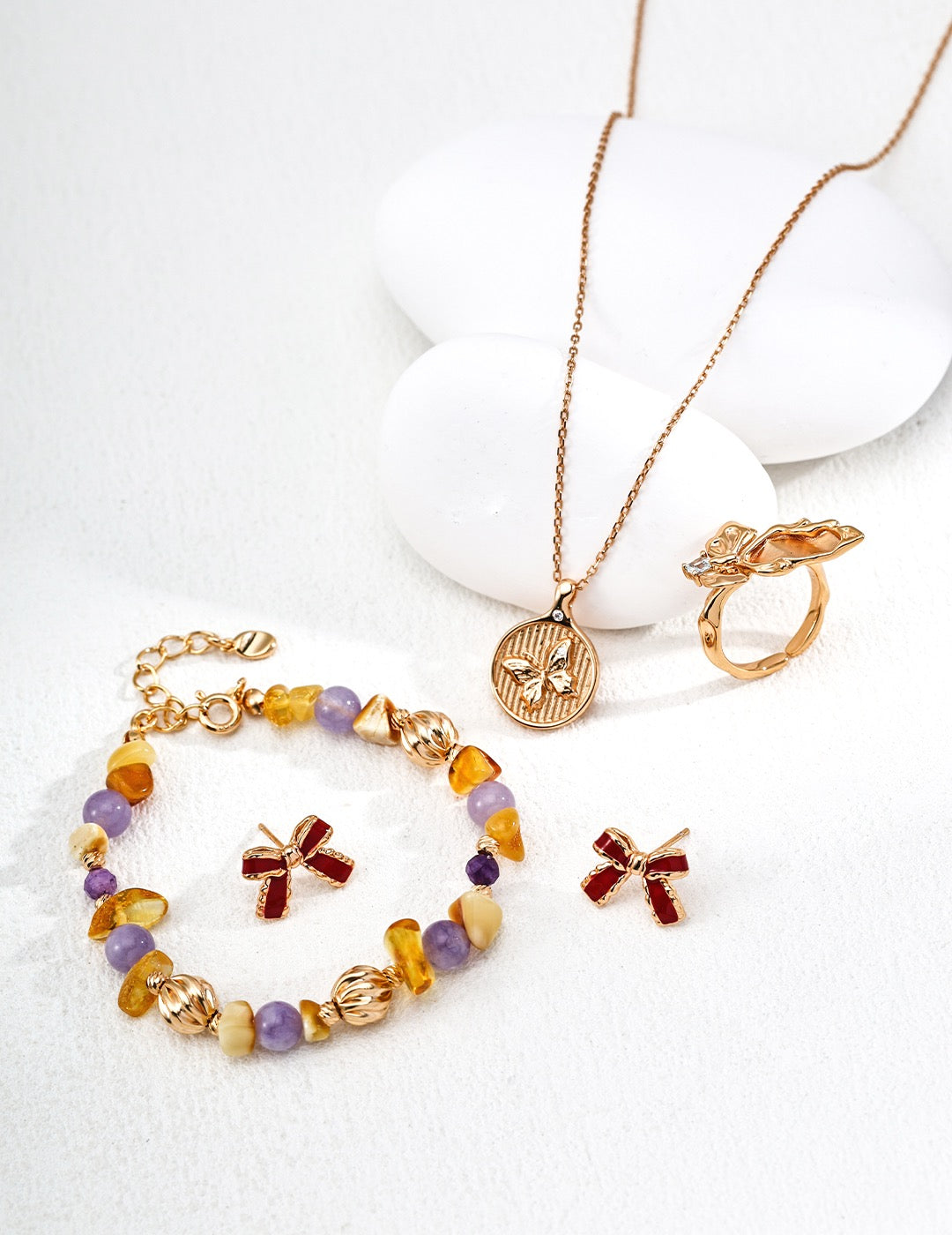 Gold bracelet with colorful gemstones and charms, necklace, and ring on a white background