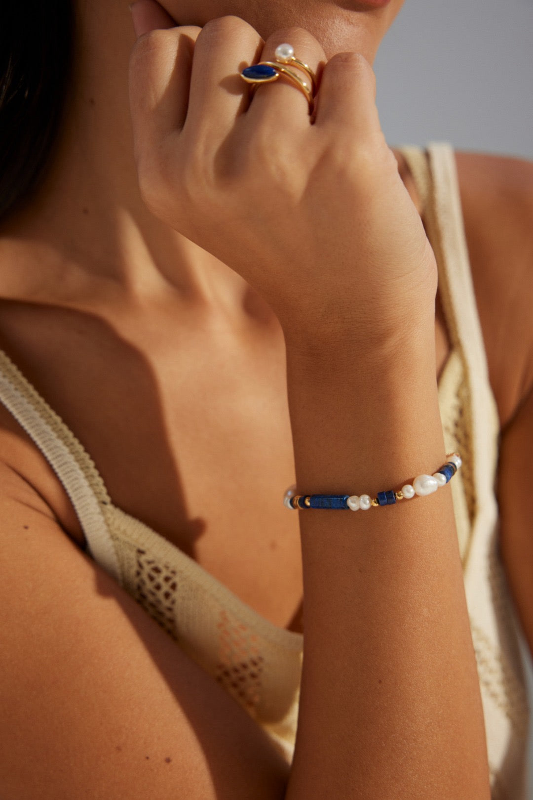 Close-up of a person's hand wearing gold rings and a bracelet with pearls and blue stones.