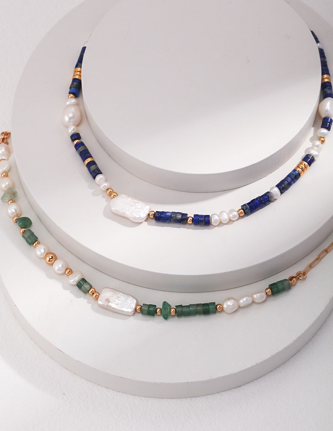 Three pearl necklaces with blue, green, and gold beads on a white surface