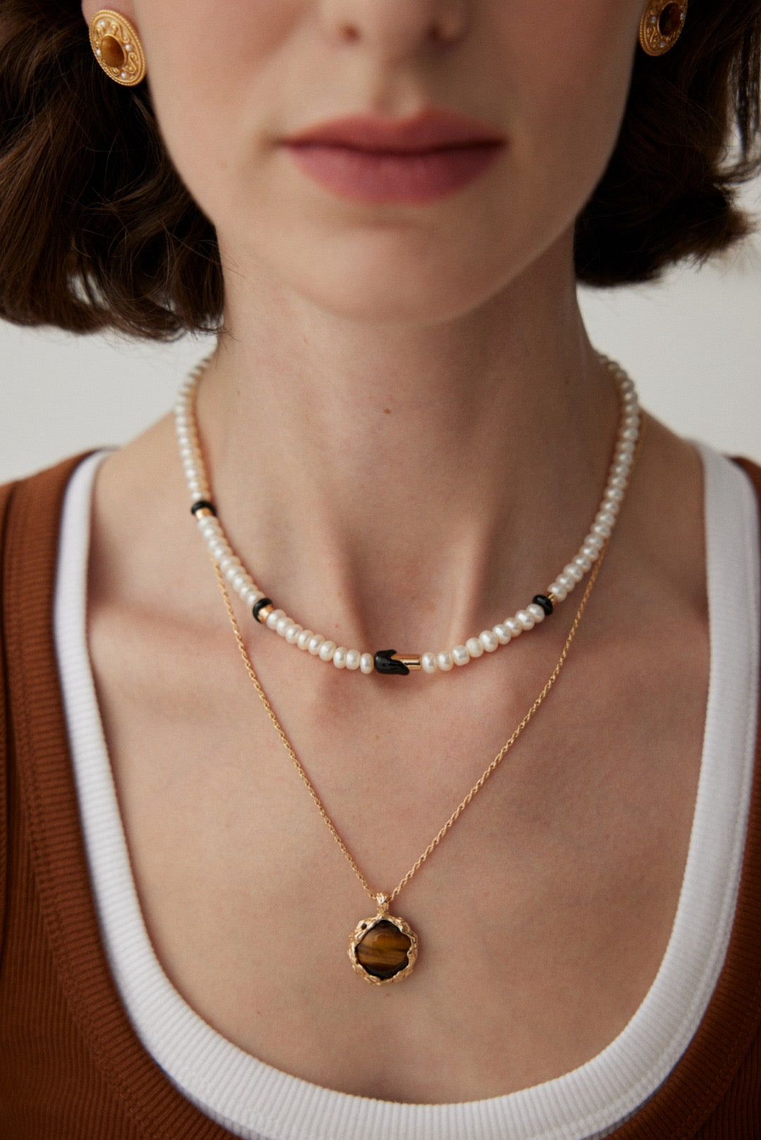 The model is wearing the Freshwater Pearl Black Enamel Necklace, which is layered with a Tiger's Eye Pendant Necklace and styled with a casual outfit.