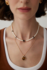 The model is wearing the Freshwater Pearl Black Enamel Necklace, which is layered with a Tiger's Eye Pendant Necklace and styled with a casual outfit.