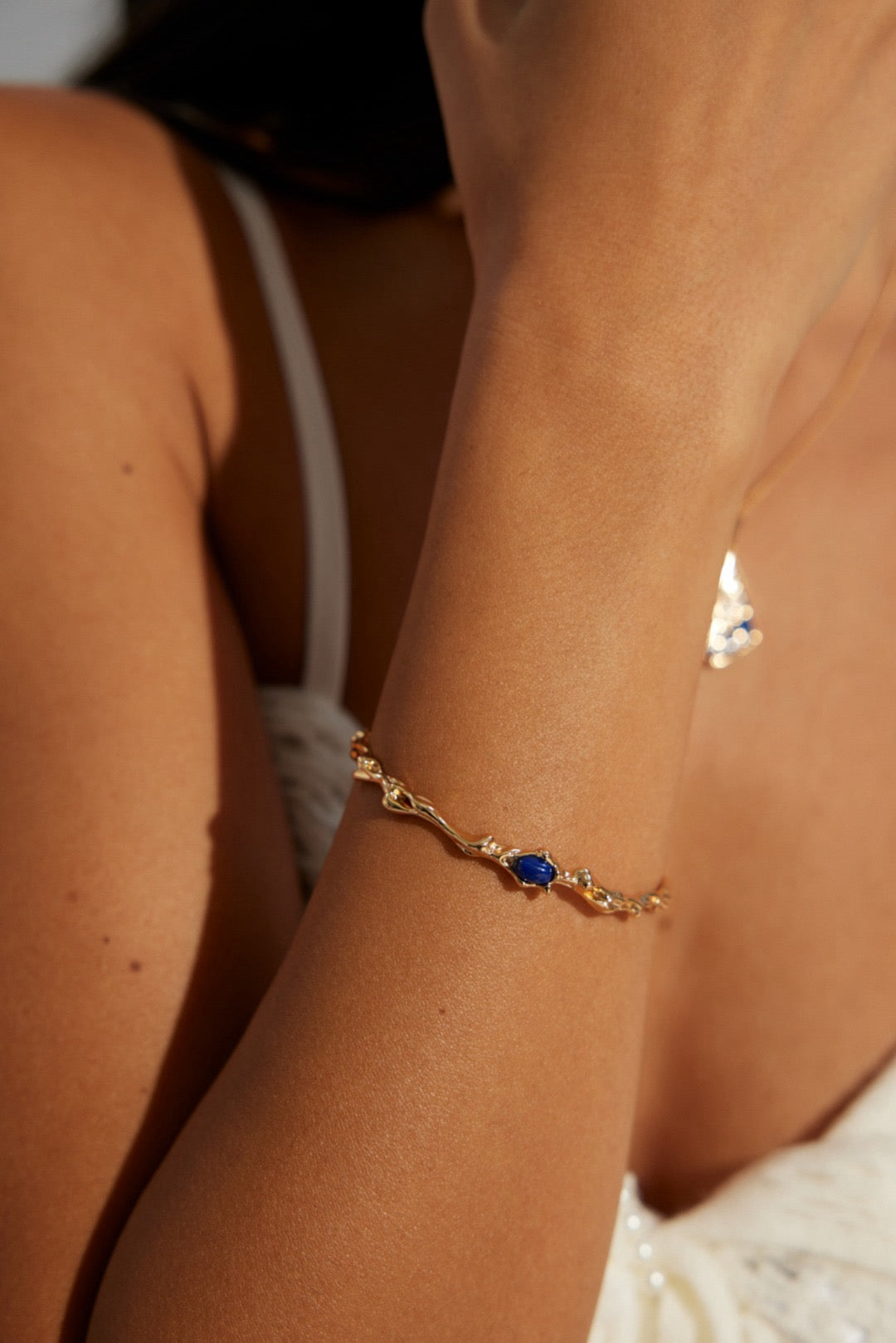 A person wearing a gold bracelet with a lapis lazuli centerpiece on their wrist.