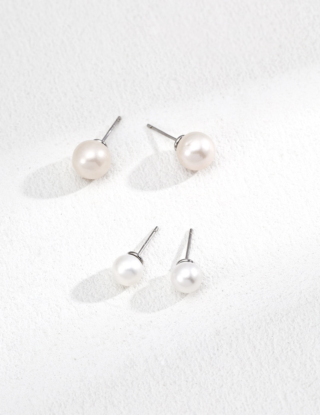 Set of pearl earrings on a textured white surface