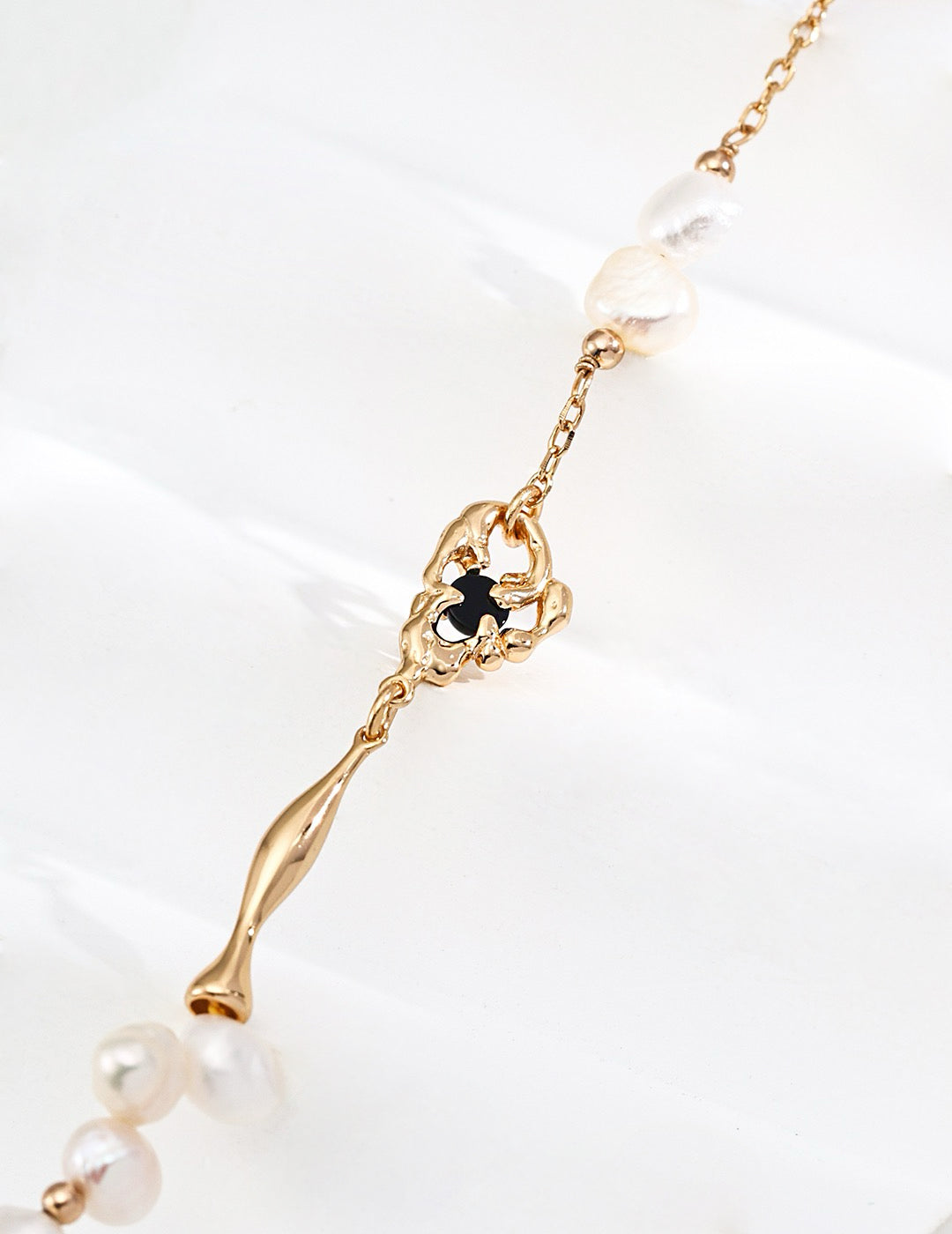 Close-up of an Aurora Freshwater Pearl Necklace featuring a detailed black agate pendant surrounded by organic gold shapes, paired with freshwater pearls strung along a dainty gold chain.