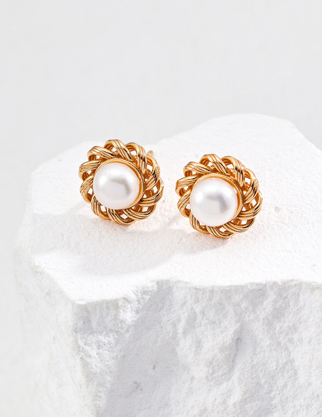 Pair of gold hoop earrings with pearl center on a white stone surface