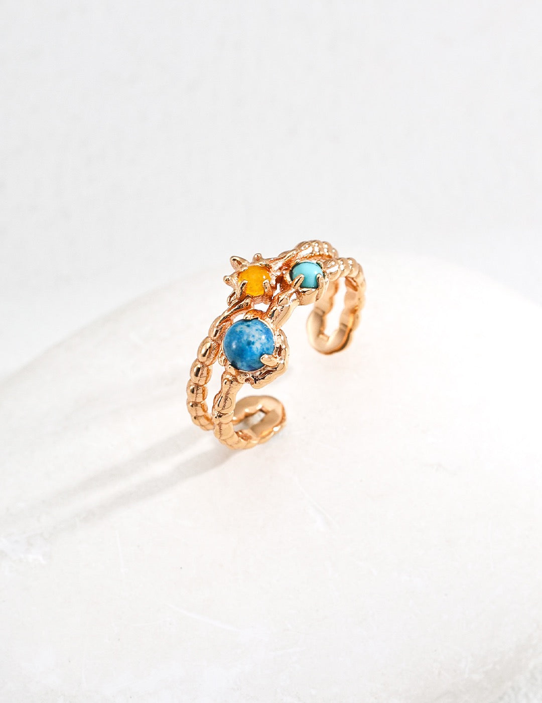 Gold ring with blue and yellow gemstones on a white background
