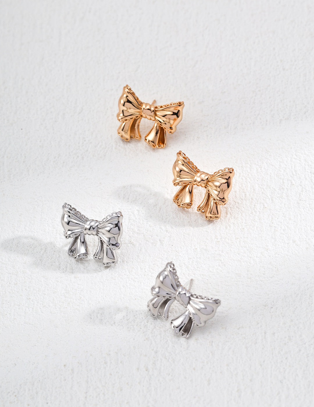 Bow-shaped earrings in rose gold and silver on a white background