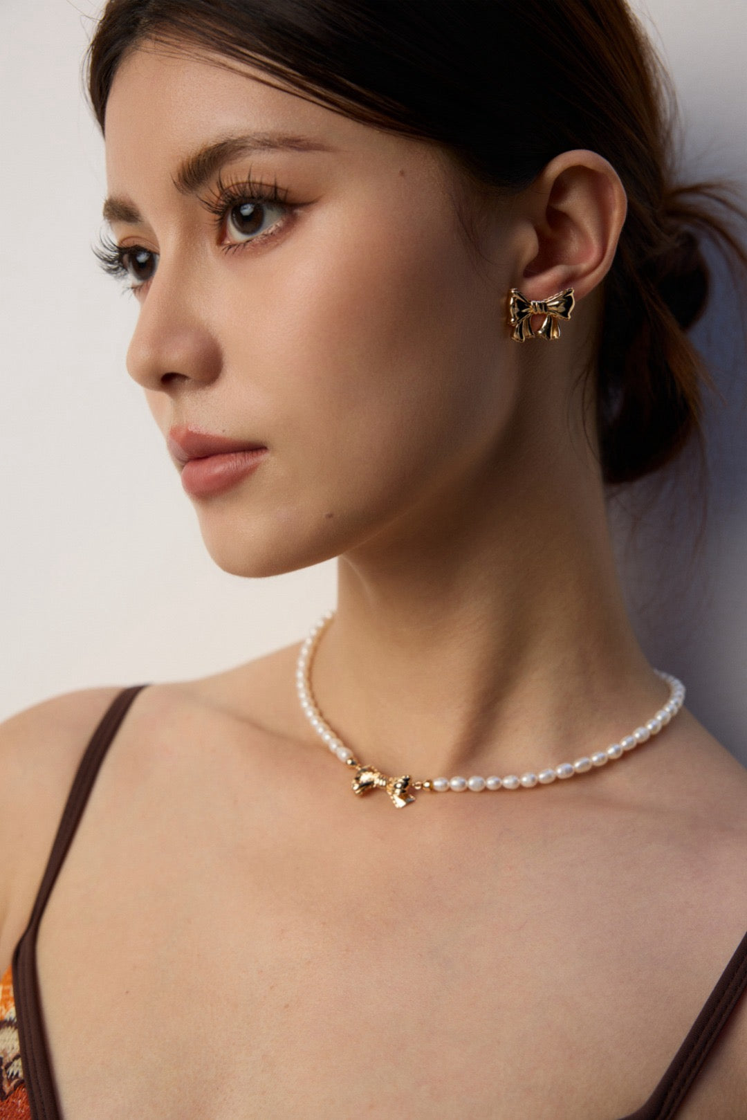 Woman wearing a pearl necklace with gold accents against a neutral background