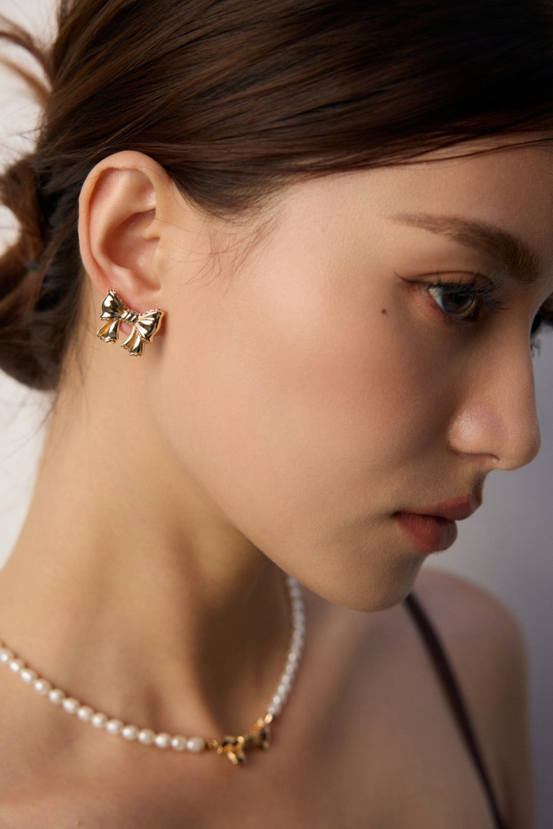Close-up of a woman wearing gold bow earrings and a pearl necklace.